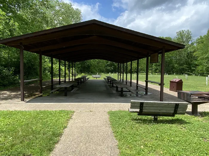 Lane Spring Recreation Area — A view of an open sided pavilion with picnic tables, pedestal BBQ grill, and benches with a background of green vegetation.