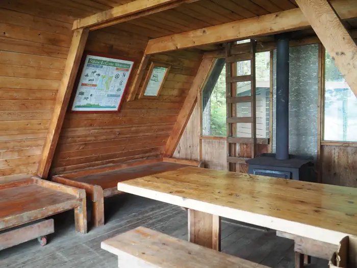 Mallard Slough Cabin — Interior of wood cabin showing 2 wood bunks, table, stove and ladder up to loft