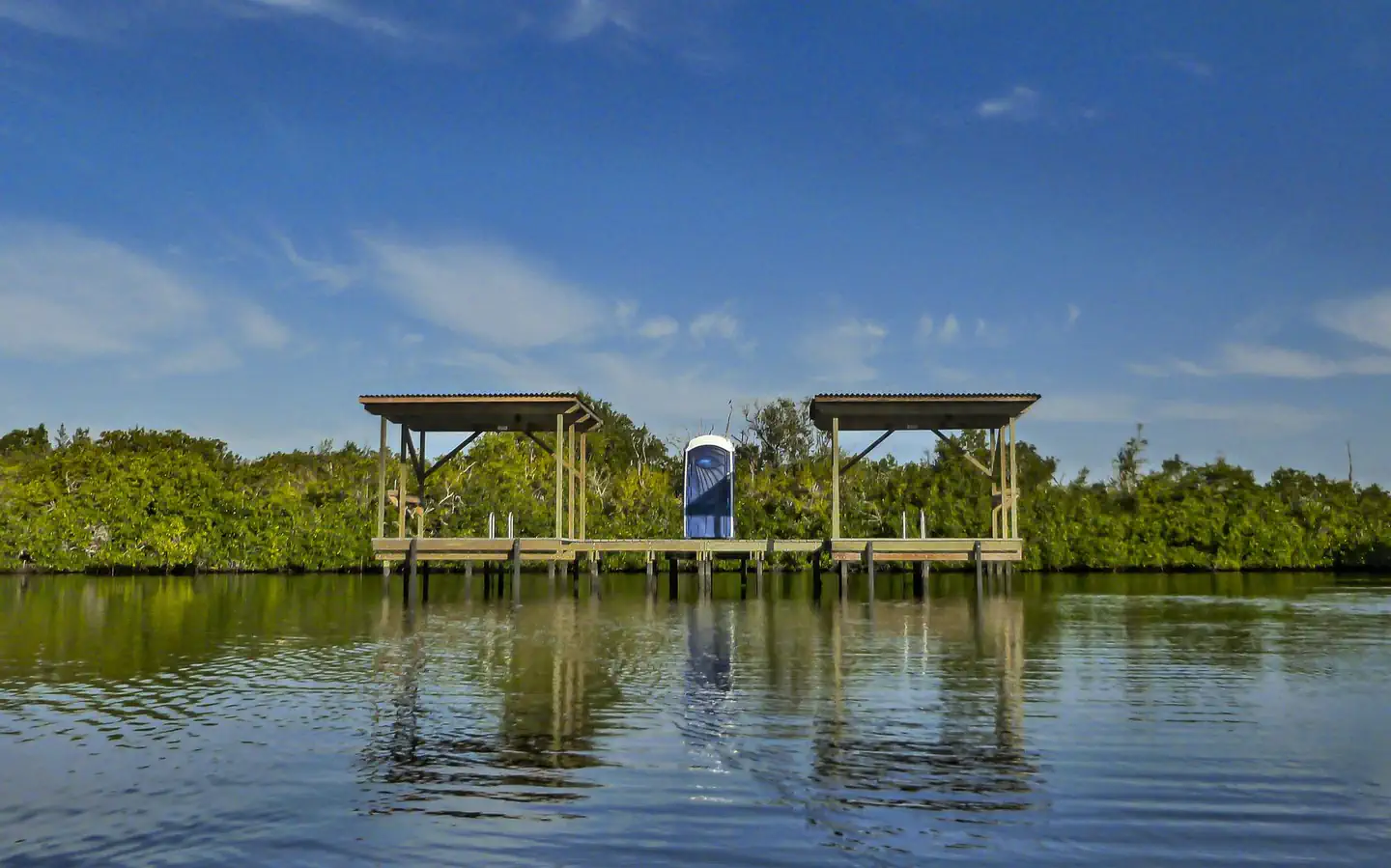 Everglades Backcountry Wilderness Camping Permits — Two roofed, wooden platforms above the water joined by a narrow bridge. A blue portable toilet is on the bridge between the two platforms.