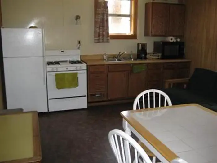 Horsethief Cabin — Kitchen with table, medium fridge and upper freeze next to electric stove, microwave and coffee maker on counter.