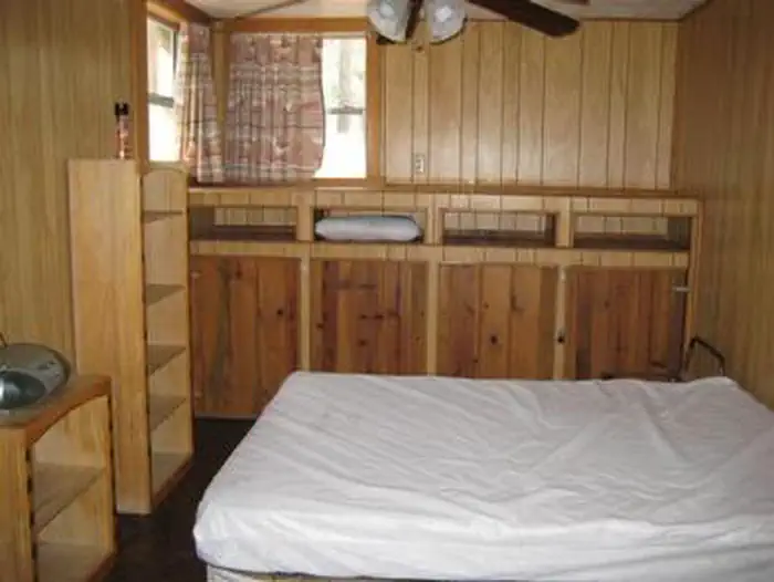 Horsethief Cabin — Horsethief Cabin bedroom with full bed, bookcases at the foot, two windows, ceiling fan and cabinets on back wall.