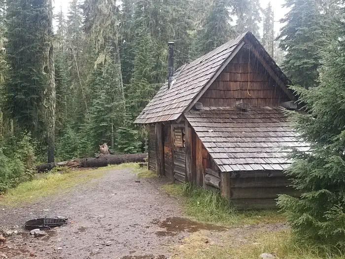 Timpanogas Lake Campground — Fire ring in front of log cabin with attached, covered wood shed in the forest.