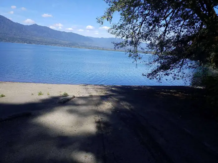 Willaby Campground — Shaded boat ramp leading to blue, sunlit lake with mountains and clouds floating in blue sky as backdrop.