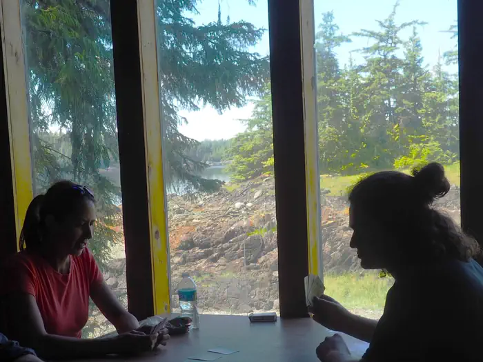 Steamer Bay Cabin — Two people play cards in shadow with view out of Steamer Bay Cabin window visible