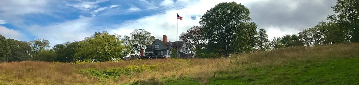 Sagamore Hill National Historic Site — A gray house a top a grassy hill with blue sky and clouds in the background.