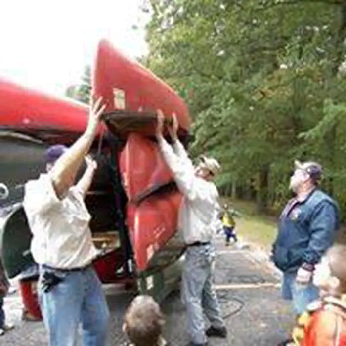 West Hill Dam — Adults and youth taking red canoes down from trailer for short walk to the Kayak/Canoe Water Trail.