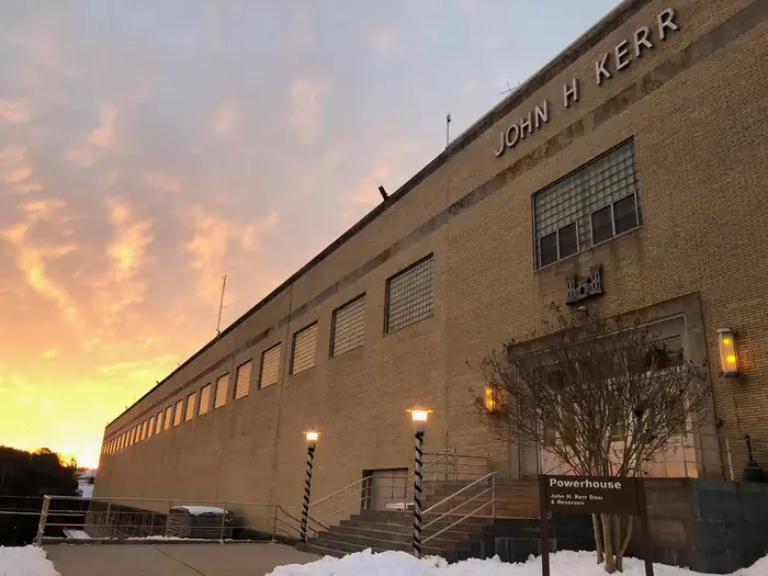 John H. Kerr Dam and Reservoir — This is a picture of the John H Kerr Dam Powerhouse with the sun rising above it. There is snow on the ground. 