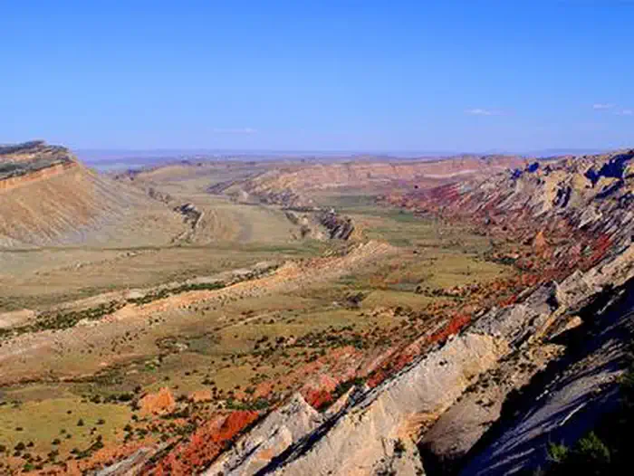 Capitol Reef National Park — A green valley, a brown ridge cuts through it. Red and brown cliffs slope up on the right side of image. The sky is a bright, cloudless blue.