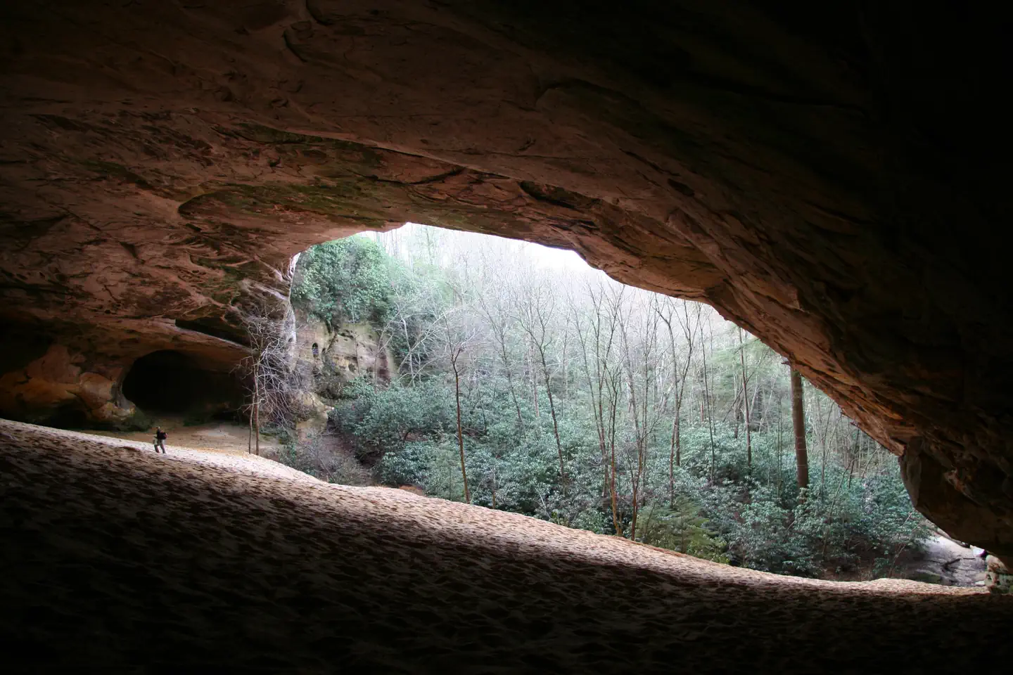Cumberland Gap National Historical Park — A man hikes in an enormous open cave with a sandy floor.