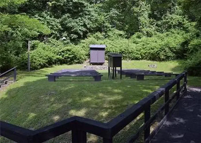 Owens Creek Campground - Catoctin Mountain Park: Campground amphitheater. Wooden boardwalk leading to open grass area with 10 wooden benches facing wooden projection screen. Dense green vegetation is behind theater.