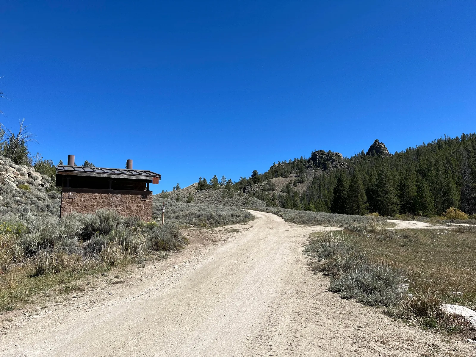 Sweetwater Bridge Campground: View of double vault toilets and road leading to two drive-up campsites