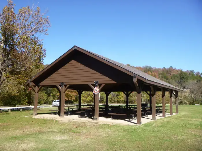 Ozark Campground - Buffalo National River: Front view of the covered pavilion with picnic tables surrounded by a grassy field. Green trees beginning to change colors are visible in the bakckground.