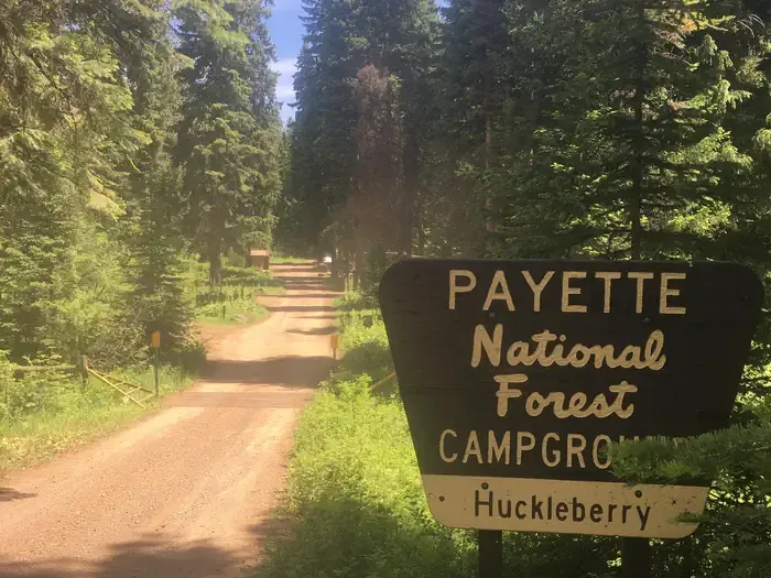 Huckleberry Campground: Dirt road with forest alongside and large sign for Huckleberry Campground.