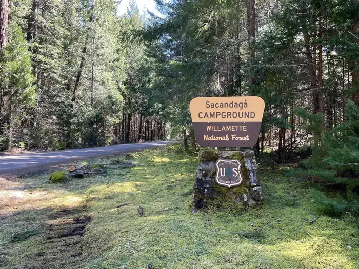 Sacandaga Campground: A cream and brown sign on a rock pedestal. The sign says " Sacandaga Campground".