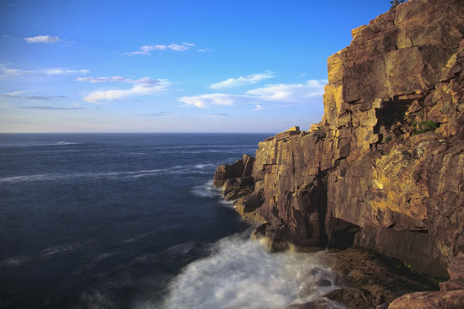 Granite sea cliff with waves breaking at its base under a blue sky