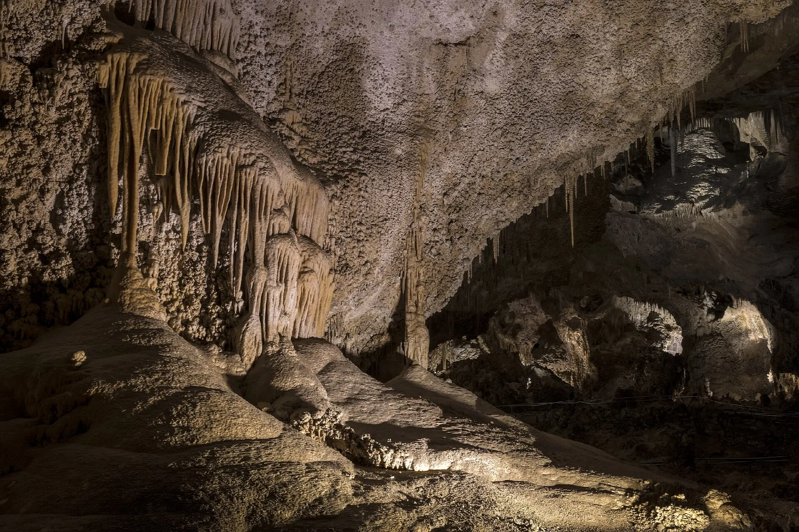 A lit trail winding past stalagmites and flowstone in a vast underground chamber