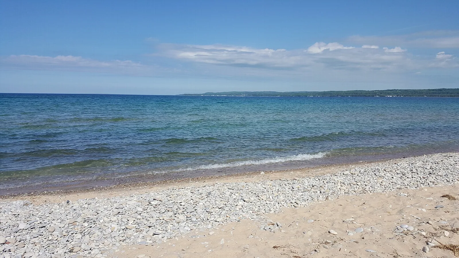 Pebbly and sandy Lake Michigan beach with blue water under a blue sky
