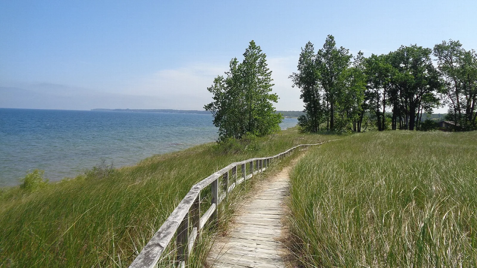 Wooden boardwalk through dune grass beside blue lake water