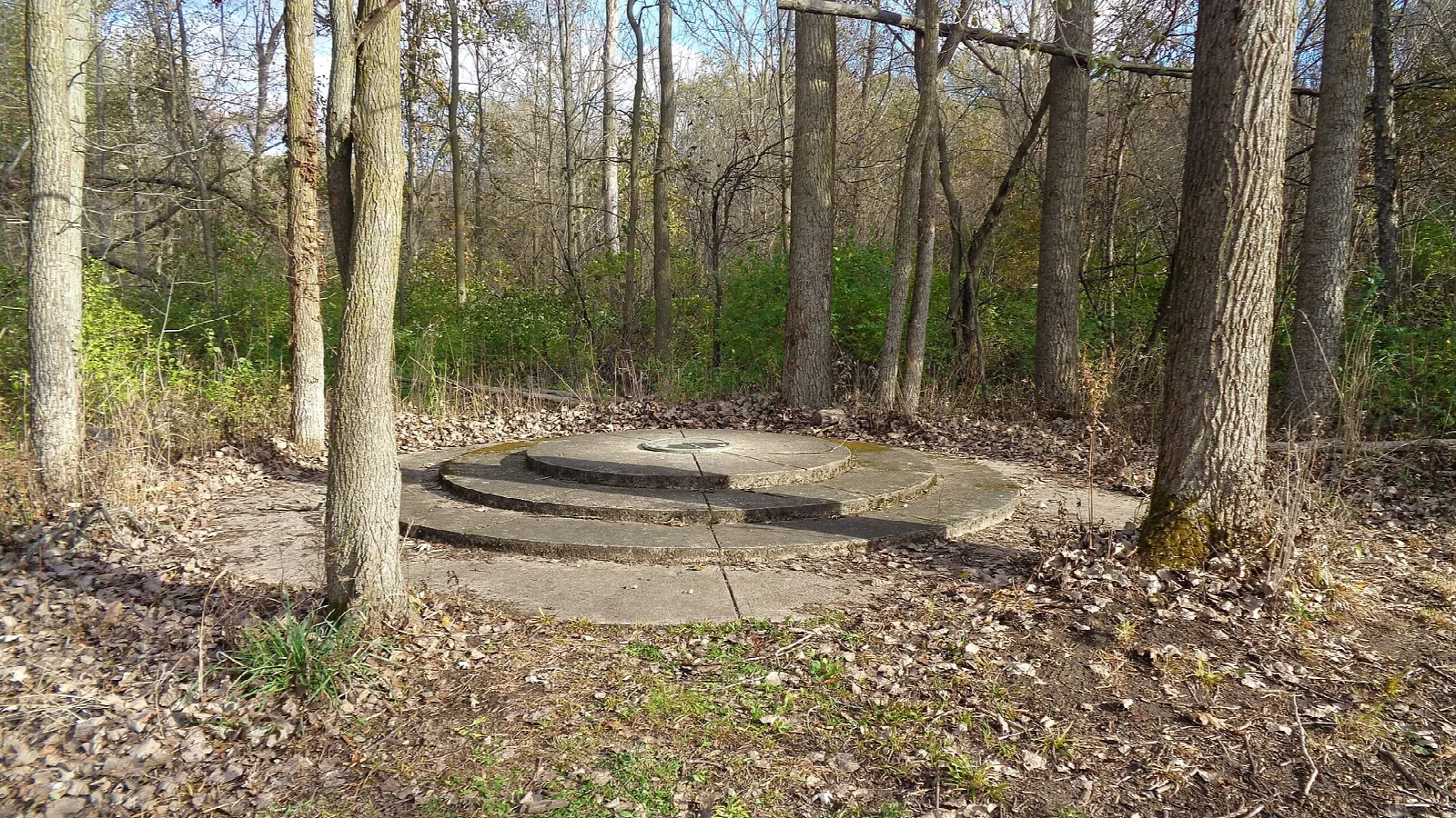 Round stepped stone platform among trees in autumn woods