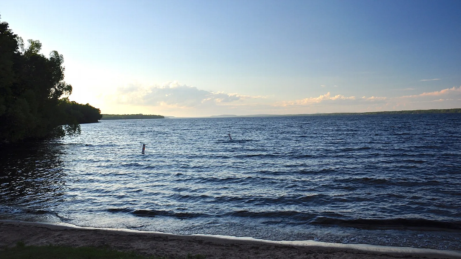Wind-rippled lake at dusk with a sandy shore and dark trees at left