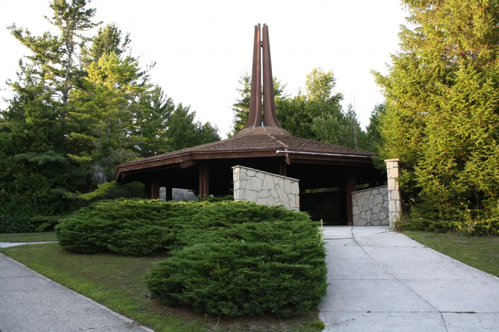 Stone and wood shelter with a tall spire, beside a paved walkway