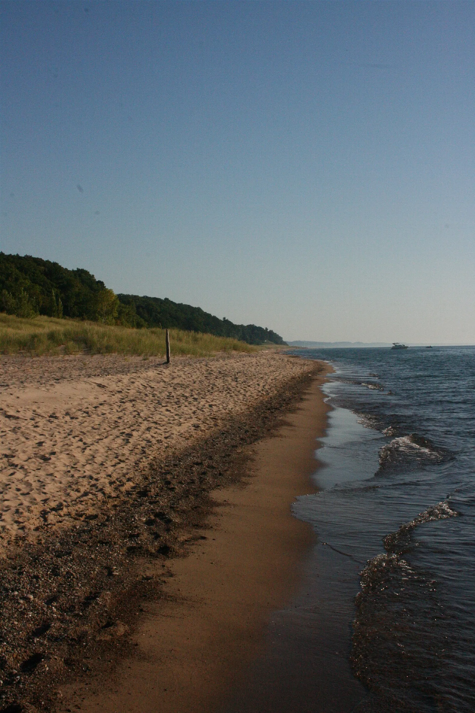 Narrow pebbly beach along calm lake water below a wooded bluff
