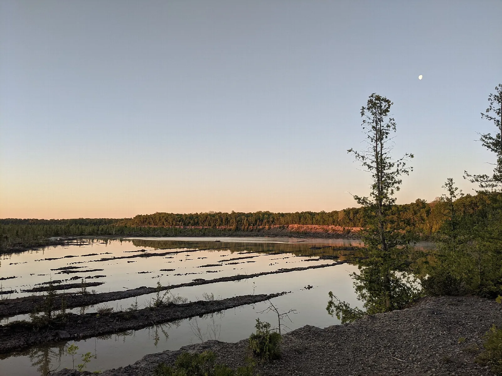 Still quarry water at dawn with a moon in a pink and blue sky