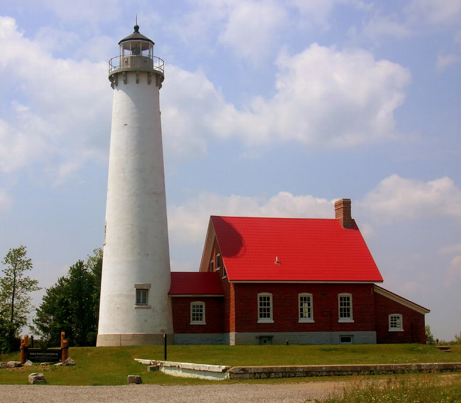 White lighthouse tower and red-roofed brick house under clouds
