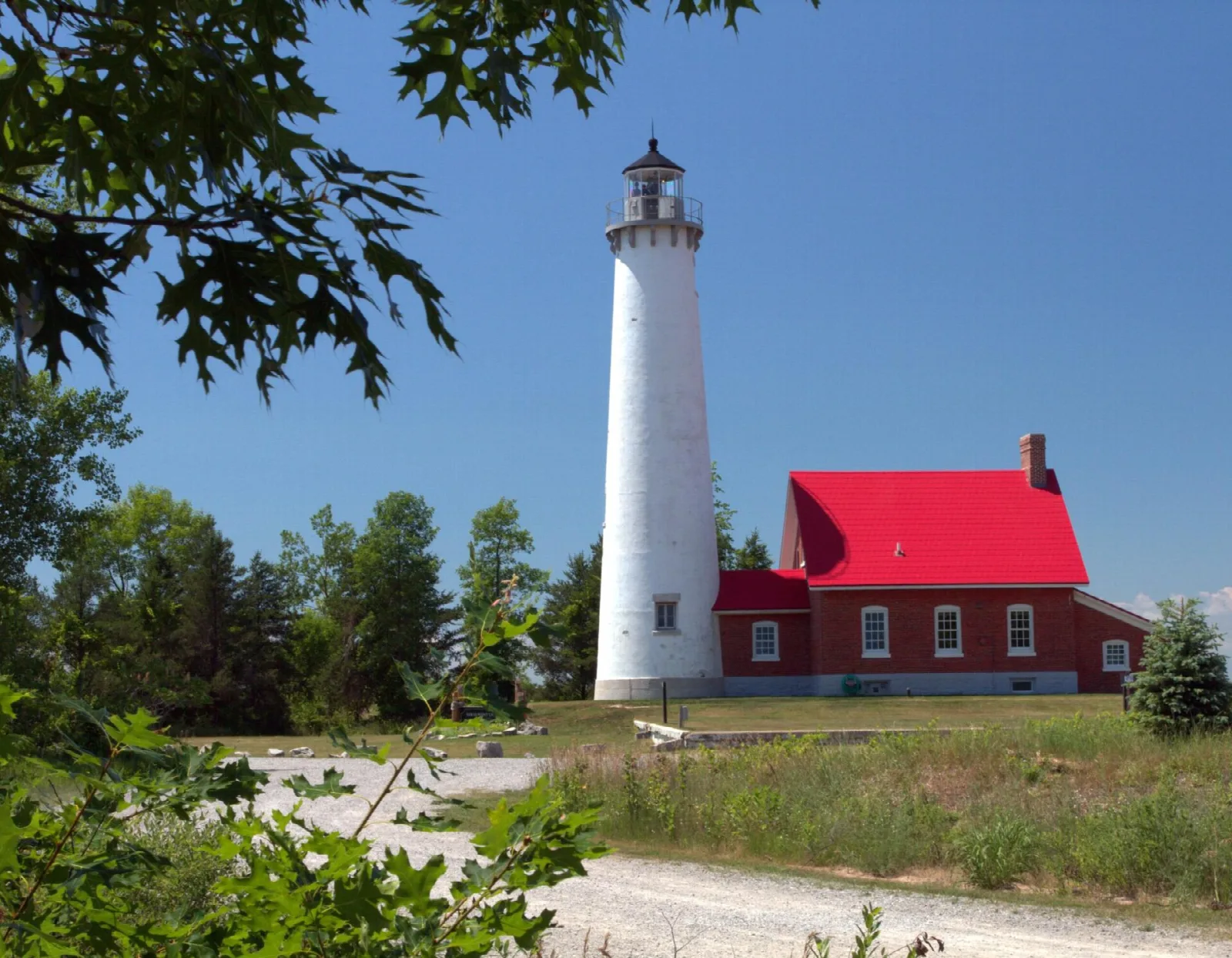 White lighthouse and red-roofed brick house with trees and gravel road