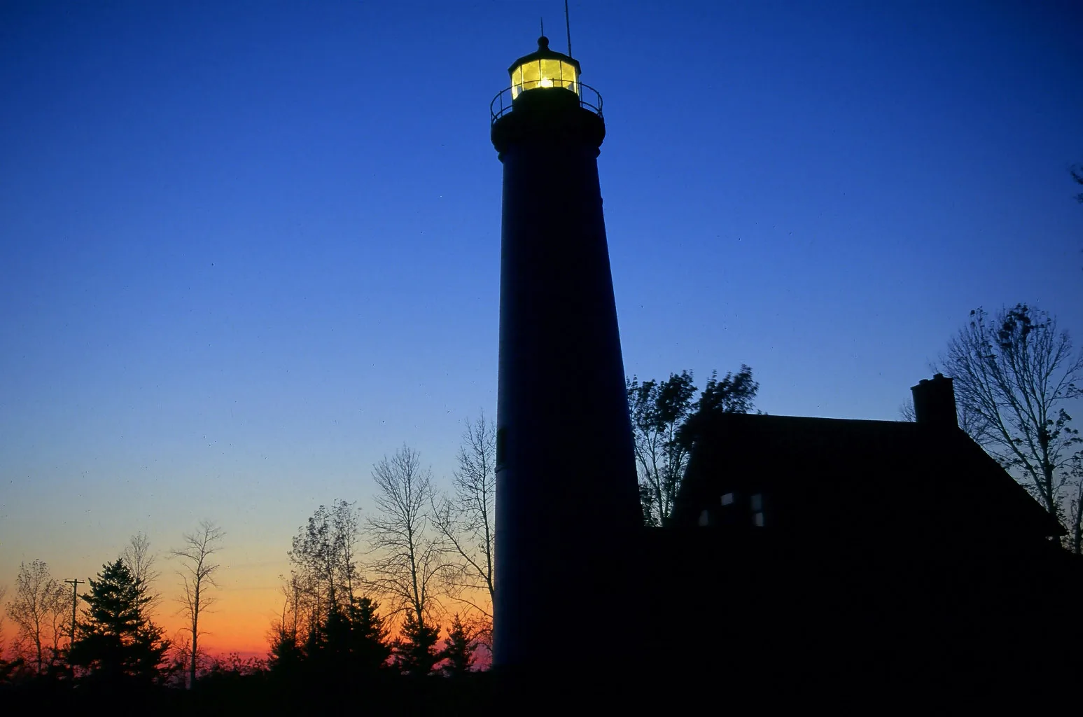 Dark lighthouse silhouette against a deep blue and orange dusk sky