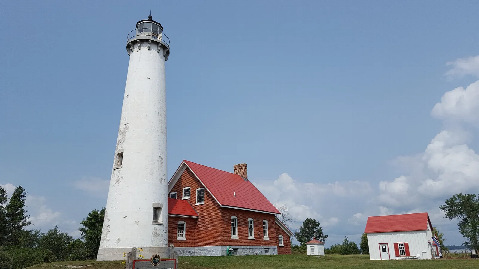 White lighthouse tower beside a brick keeper's house with red roof under a blue sky