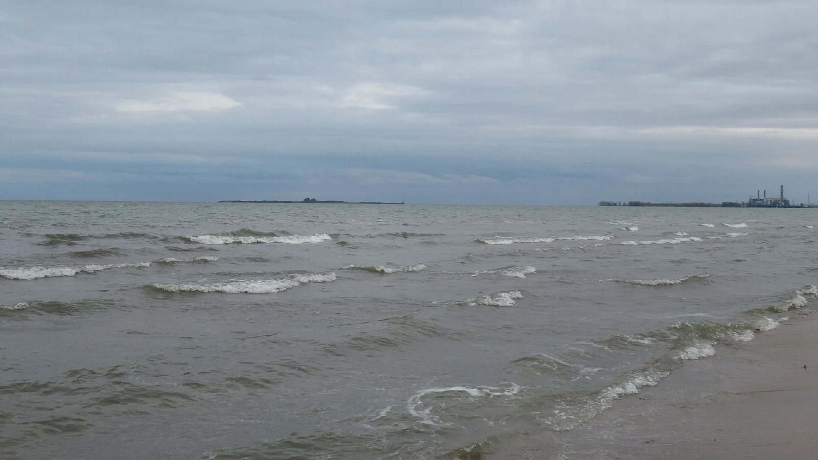 Waves rolling onto the shore of a gray bay under cloud