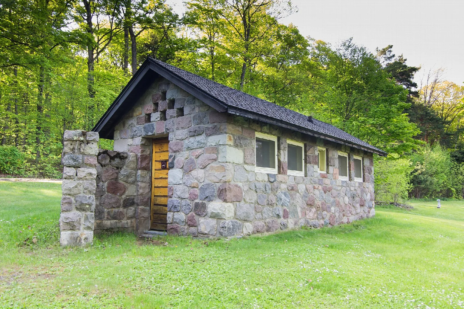 Small fieldstone building with a dark roof beside a green lawn