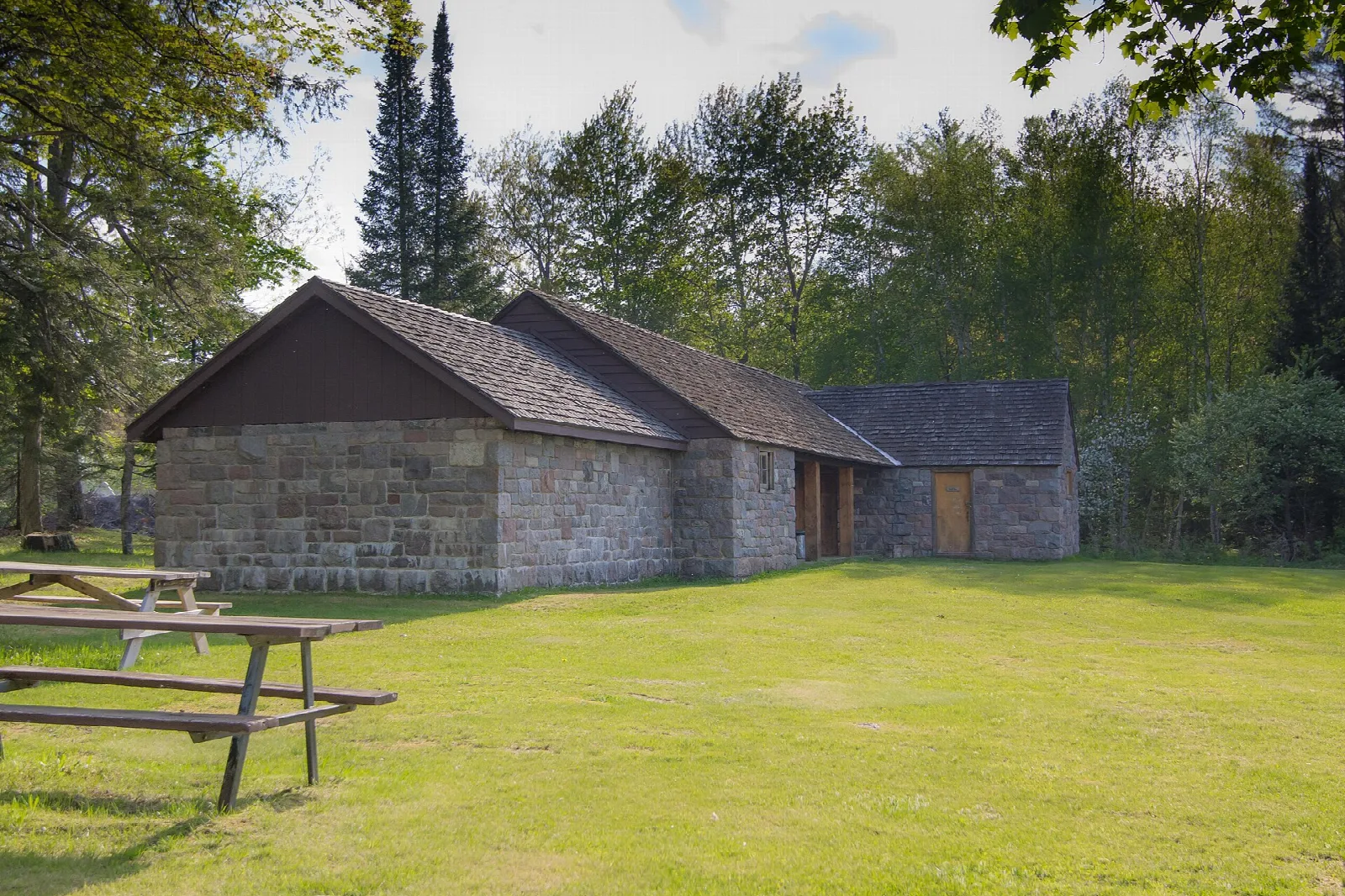 Stone and timber shelter beside a lawn and picnic tables