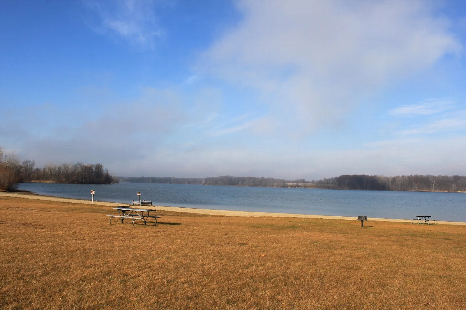 Sandy beach with picnic tables beside a lake