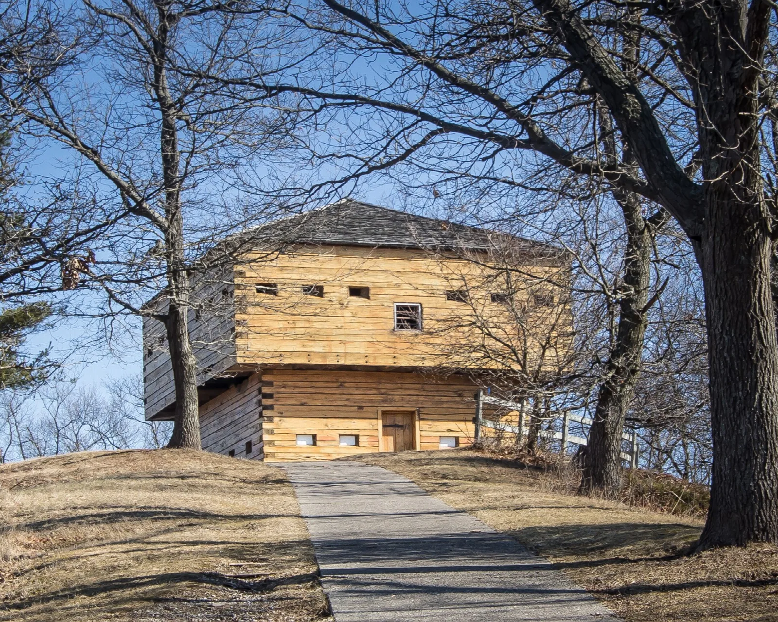 Log blockhouse among bare trees with a paved path
