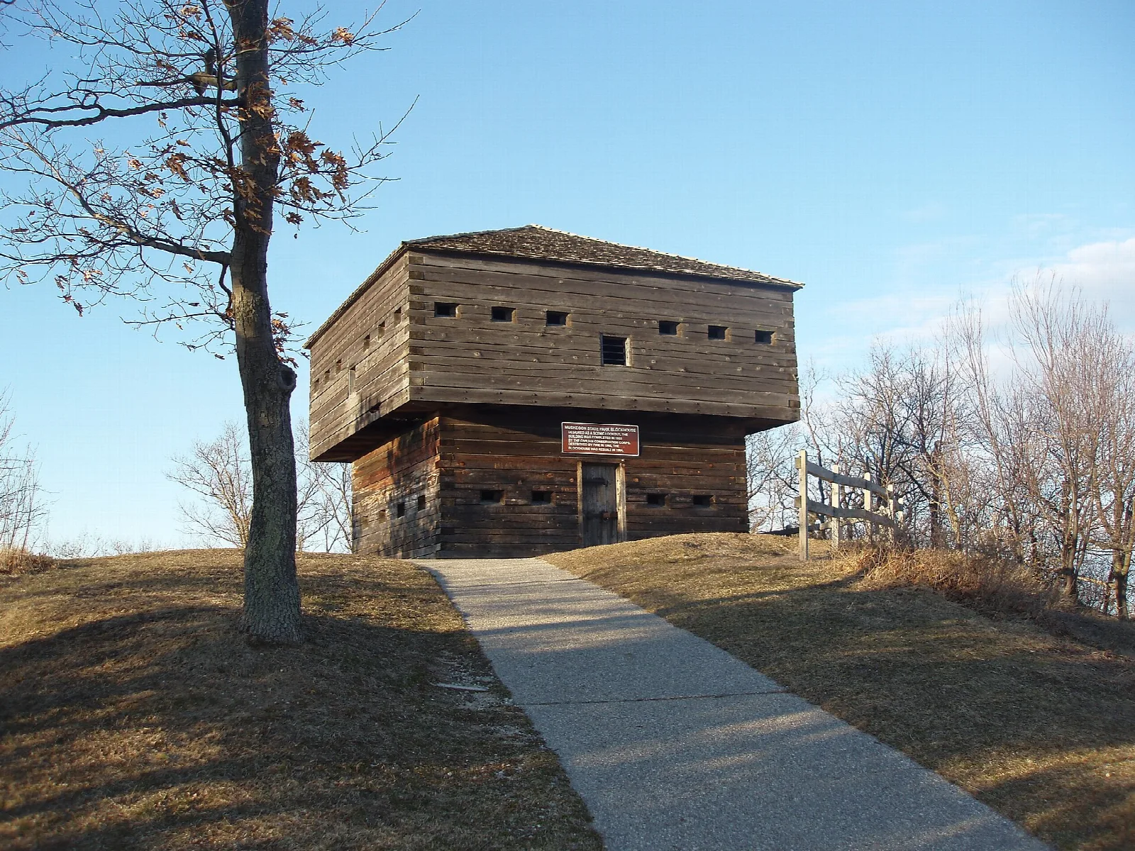 Log blockhouse on a grassy hilltop with a paved path