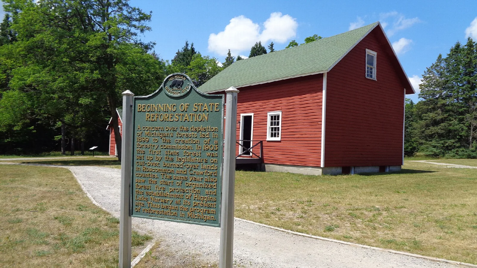Red building and historical marker on a lawn among trees
