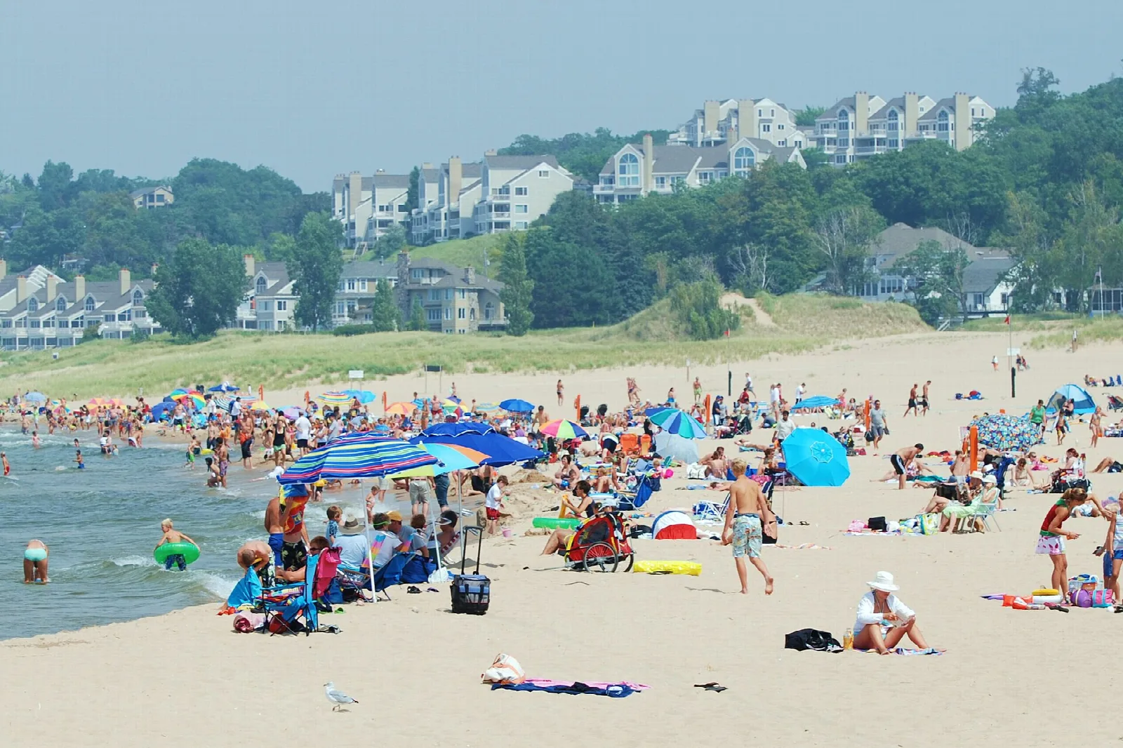 Crowded sandy beach with umbrellas and houses on the bluff behind