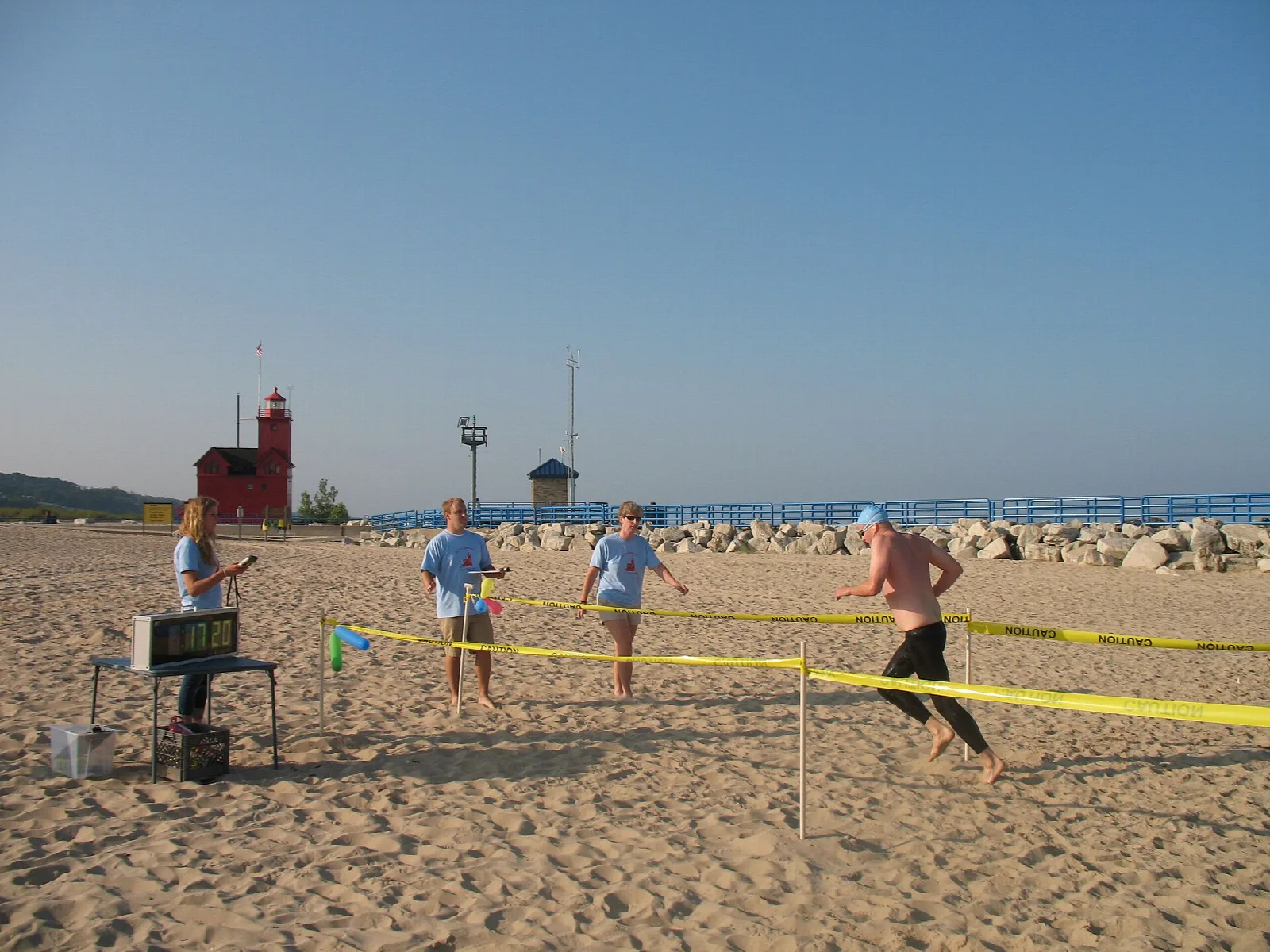 Red lighthouse beyond a sandy beach with people at a race