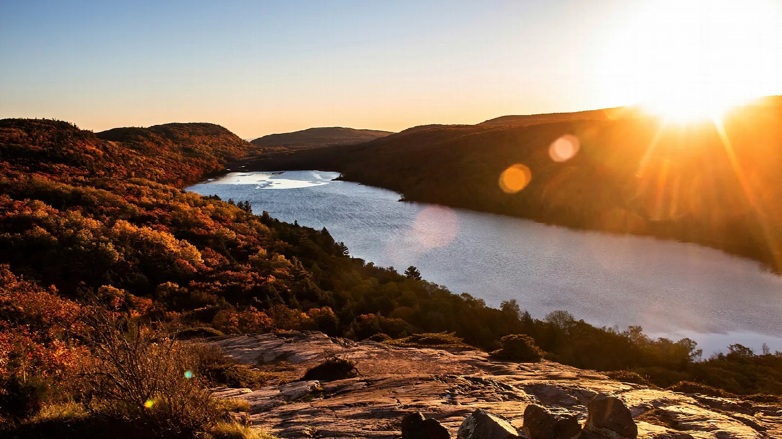 Lake at sunset between rocky hills with the sun low on the horizon