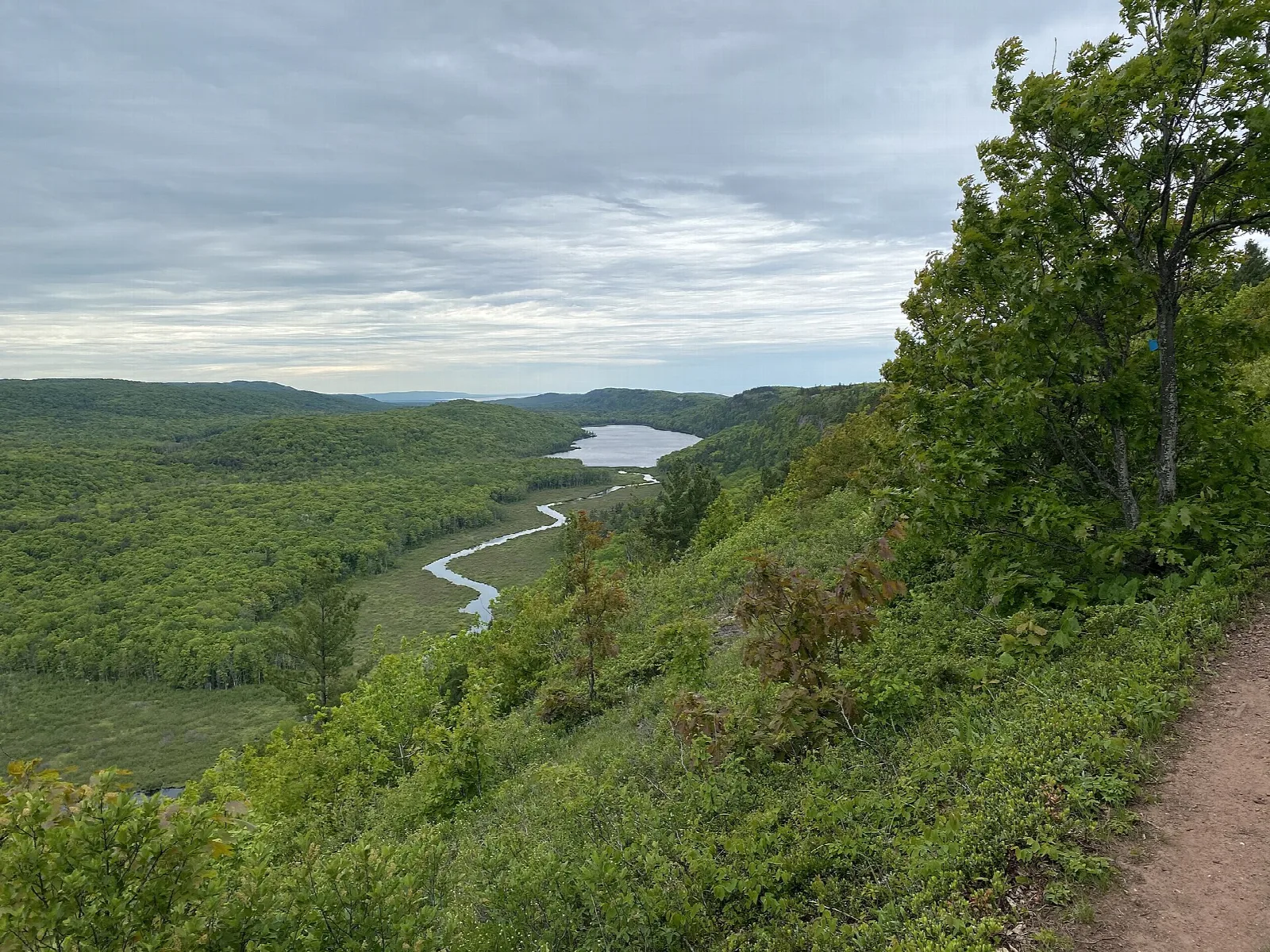 Trail along a green ridge above a river valley and lake