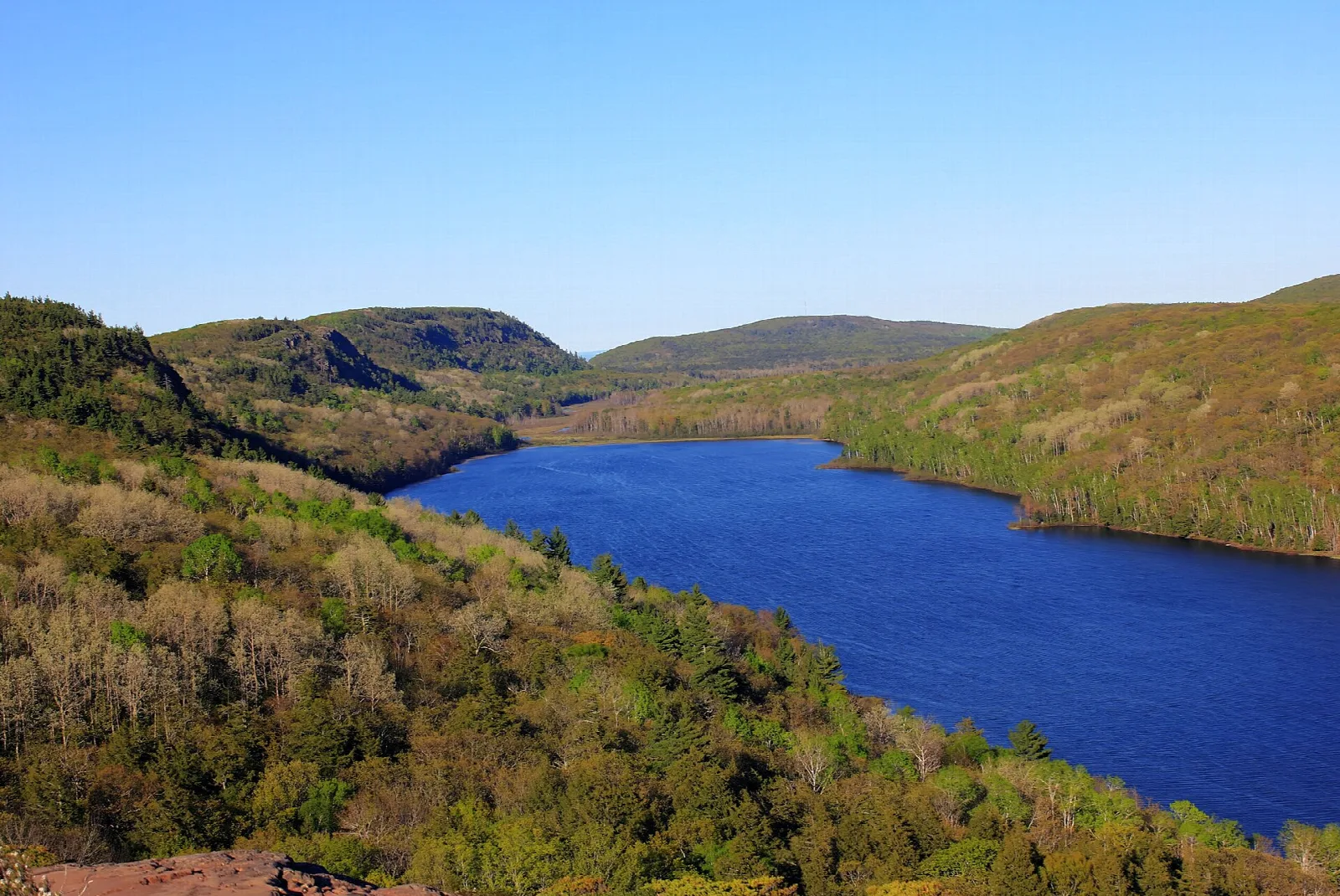 Deep blue lake below forested hills under a clear sky