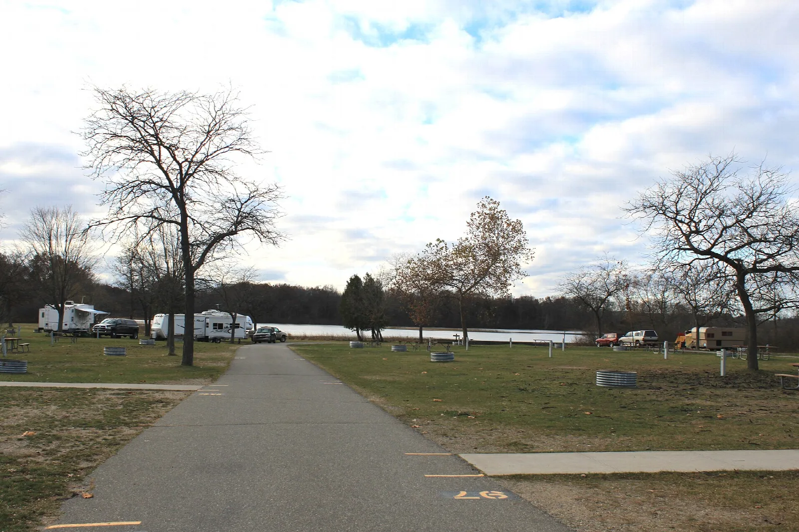 Paved path through a grassy campground with trailers by a lake