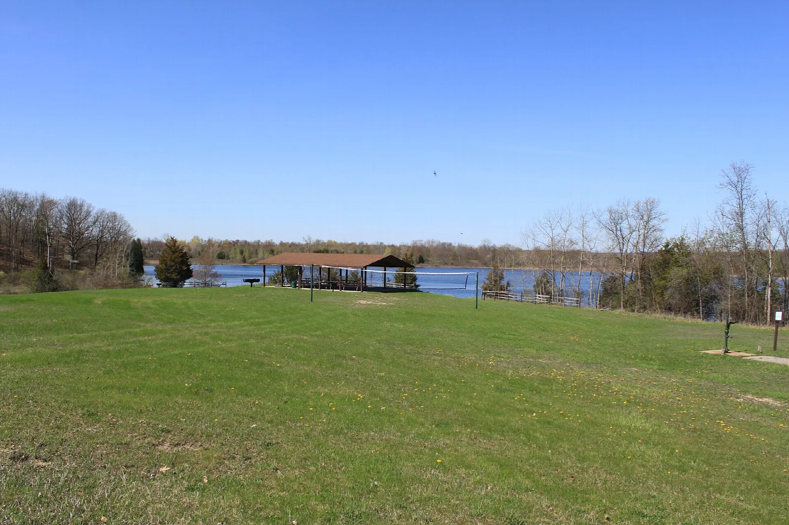 Open green lawn leading to a lake with a picnic shelter