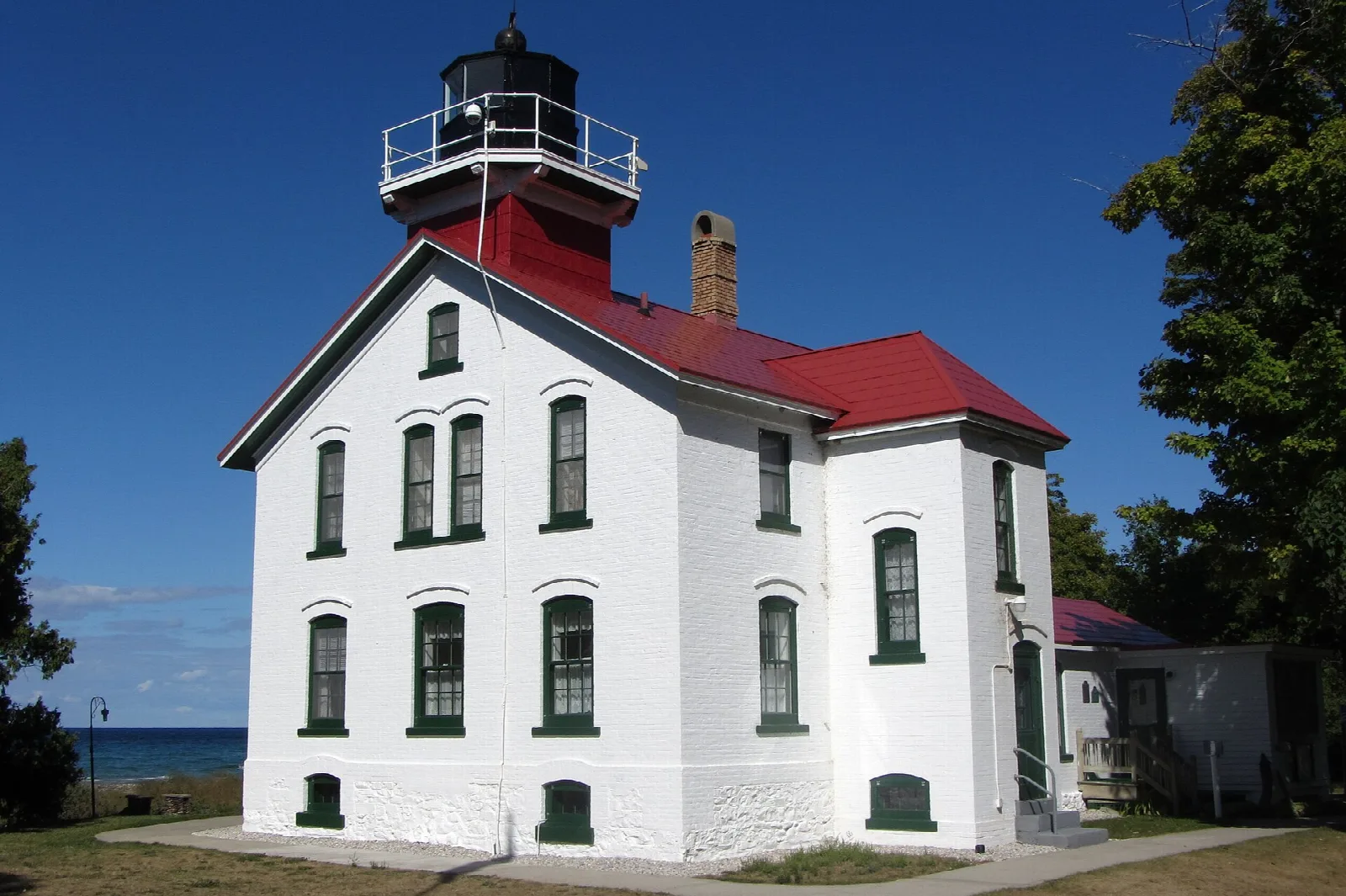 White lighthouse with a red roof and dark lantern against a deep blue sky