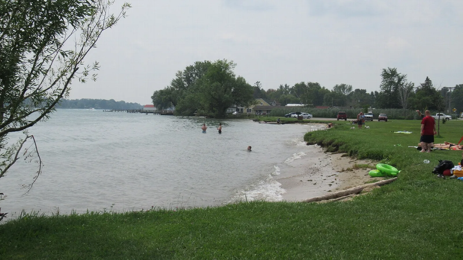 Grassy riverbank and small sand beach on the St. Clair River with people wading