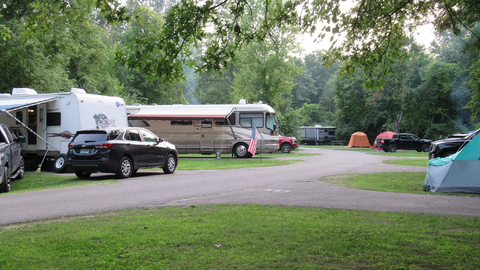 Campsites with RVs and a tent among shade trees