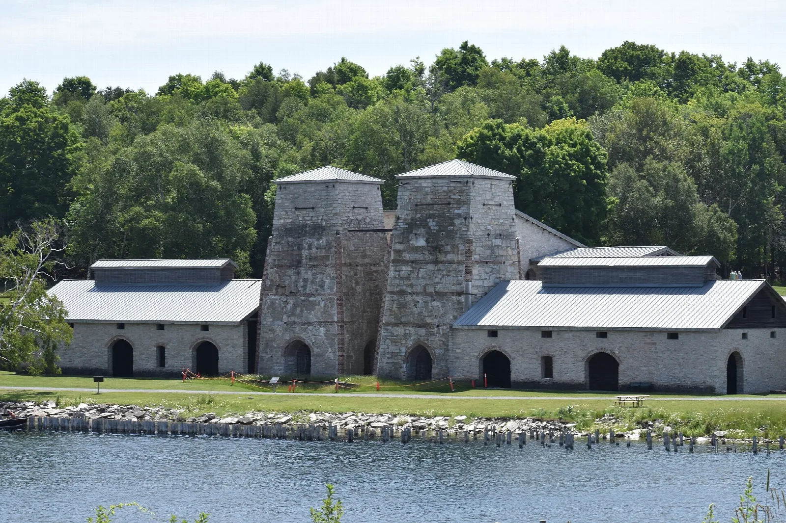 Stone furnace buildings with metal roofs beside the water