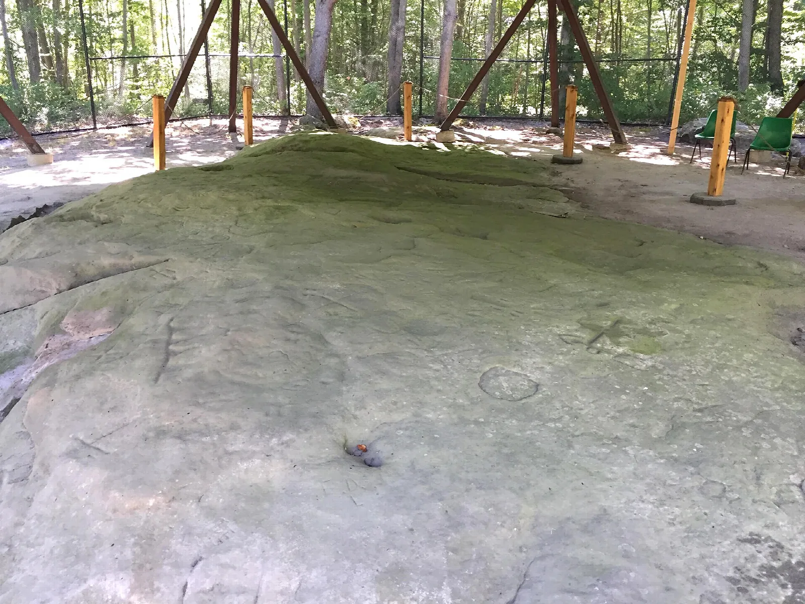 Flat sandstone outcrop with carved marks under a wooden roof frame